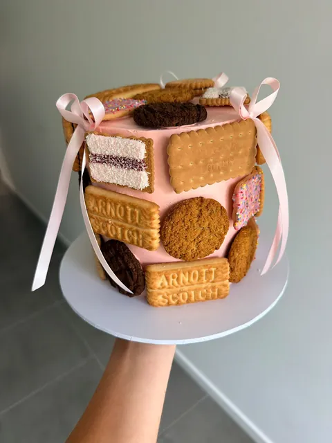Pink cake covered in classic Australian biscuits with pale pink ribbon bows