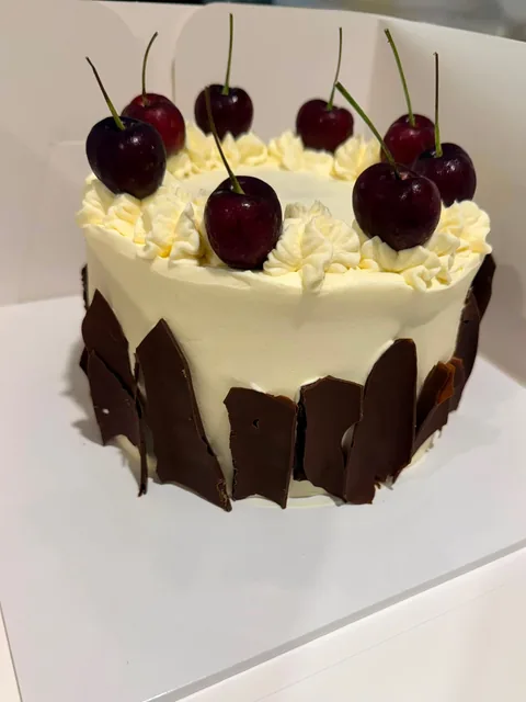 Cream buttercream cake with chocolate shards around the sides, piped rosettes and fresh cherries on top