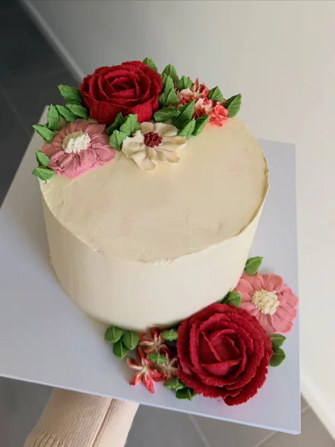 Smooth cream cake decorated with piped buttercream roses and flowers in red, pink and cream