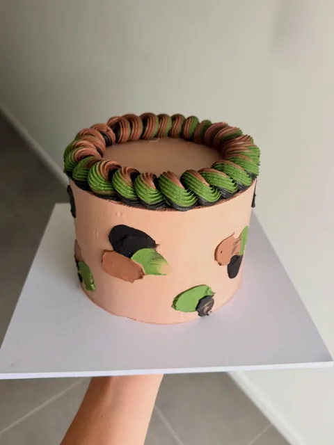 Peach buttercream cake with green, brown and black camouflage swatches and a swirled piped border