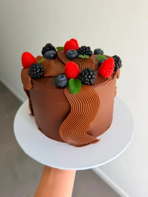 Chocolate buttercream cake with wavy piped chocolate ribbons, fresh raspberries, blackberries, blueberries and mint