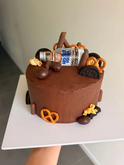 Chocolate buttercream cake topped with pretzels, Oreos, popcorn, chocolates and a mini Absolut Vodka bottle