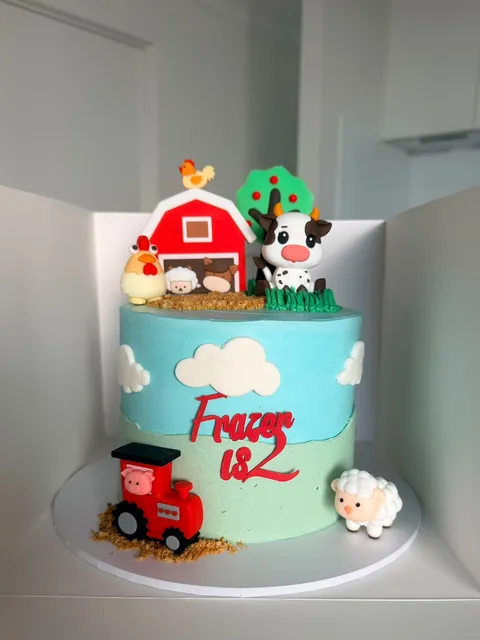 Blue and green farmyard cake with a red barn, cow, sheep, chicken and tractor for a second birthday