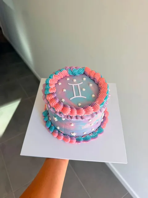 Pastel pink and blue marbled cake with coral and blue piping, white stars and the Gemini star sign on top