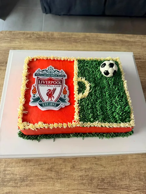 Rectangular slab cake, half red with the Liverpool FC crest and half piped green grass with a fondant soccer ball