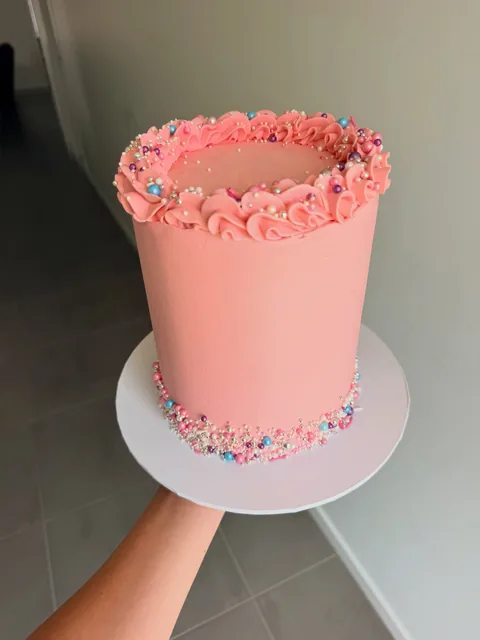 Tall pink buttercream cake with a ruffled piped top edge and pink, blue, purple and silver sprinkles