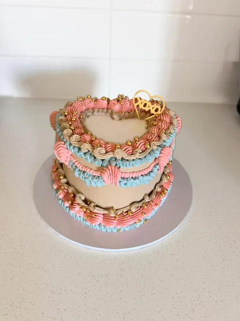 Beige vintage heart cake piped in pink and blue with gold pearls and a gold XOXO heart topper