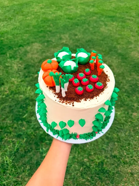 Cream buttercream cake topped with a veggie patch of chocolate crumb soil, fondant cabbages, pumpkins, carrots, tomatoes and leeks, with green leaves around the sides